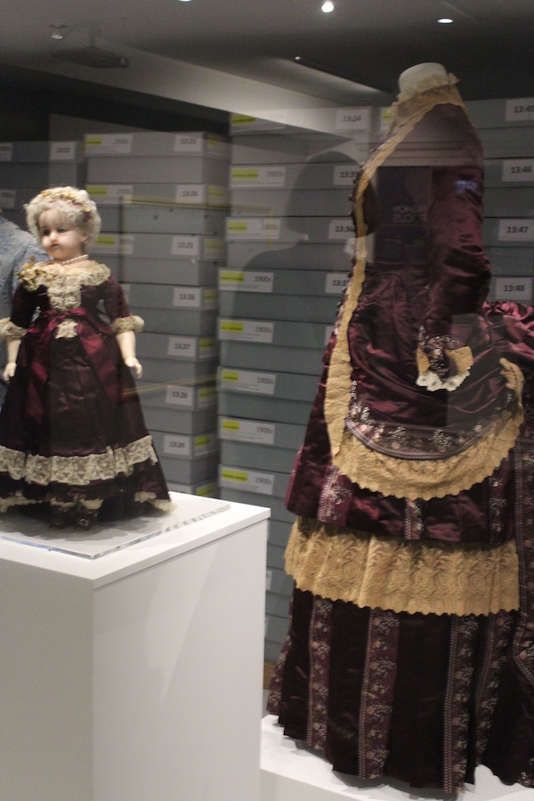 Fashion dolls, circa 1870s. Plum coloured satin dress trimmed with ecru lace.